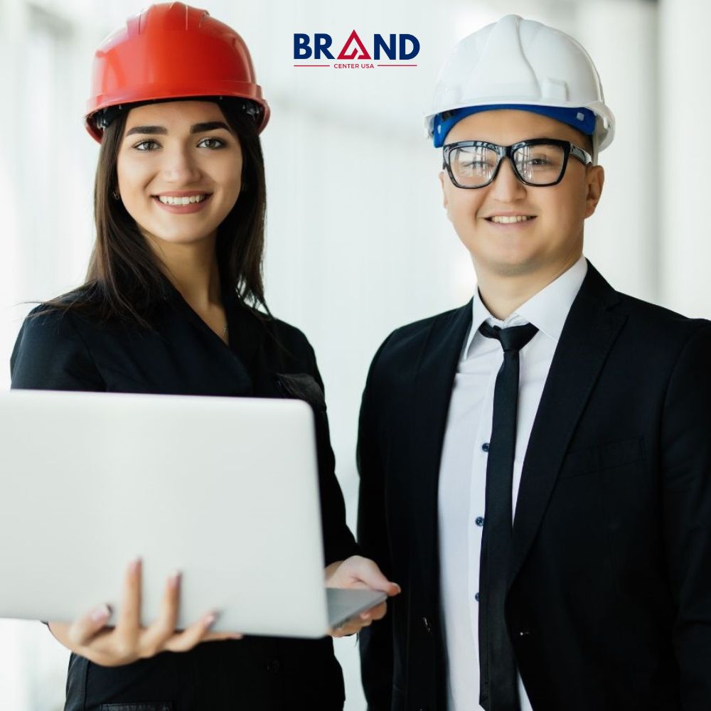 Two smiling contractors in hard hats with a laptop.