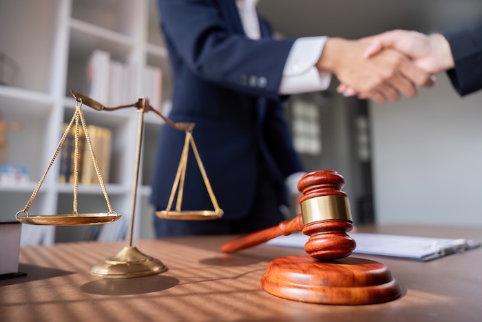 Gavel, scales of justice, and lawyers shaking hands.